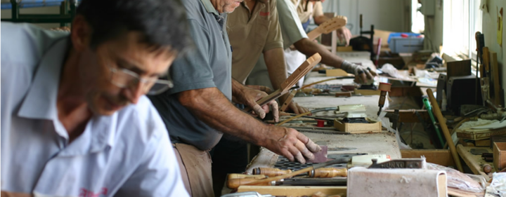A workbench with several Alhambra craftsmen working on guitars